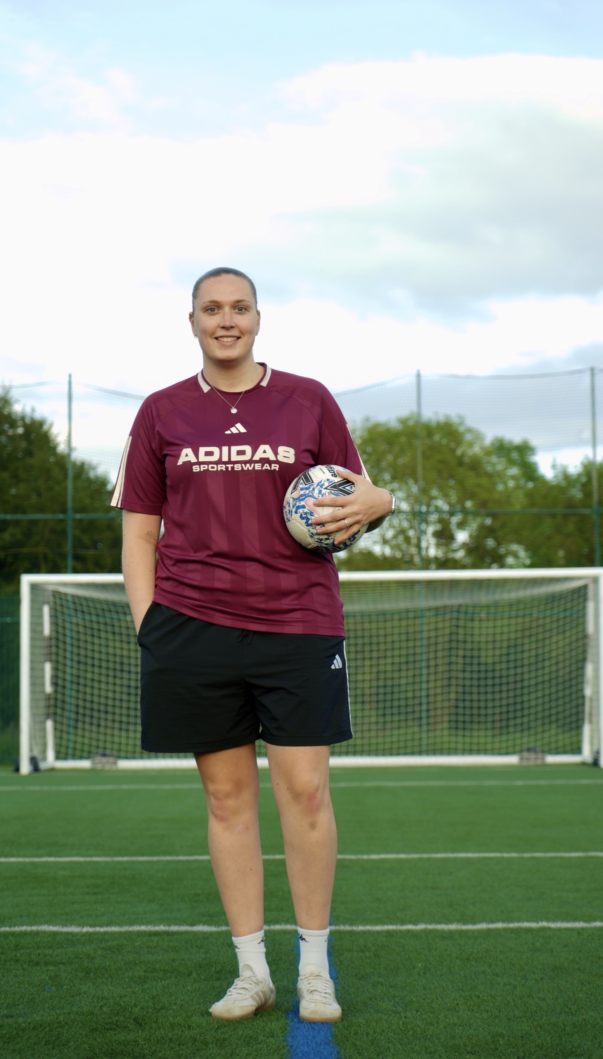 Lydia Shale standing on a football pitch smiling and holding a football.