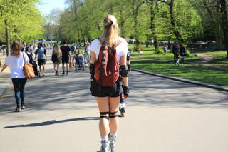 Busy path in a park with a rear view of two people rollerblading.