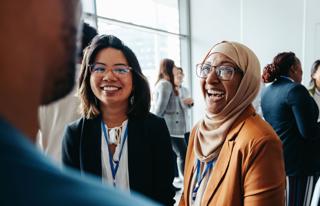 Two women face the camera at a networking event, they are smiling.