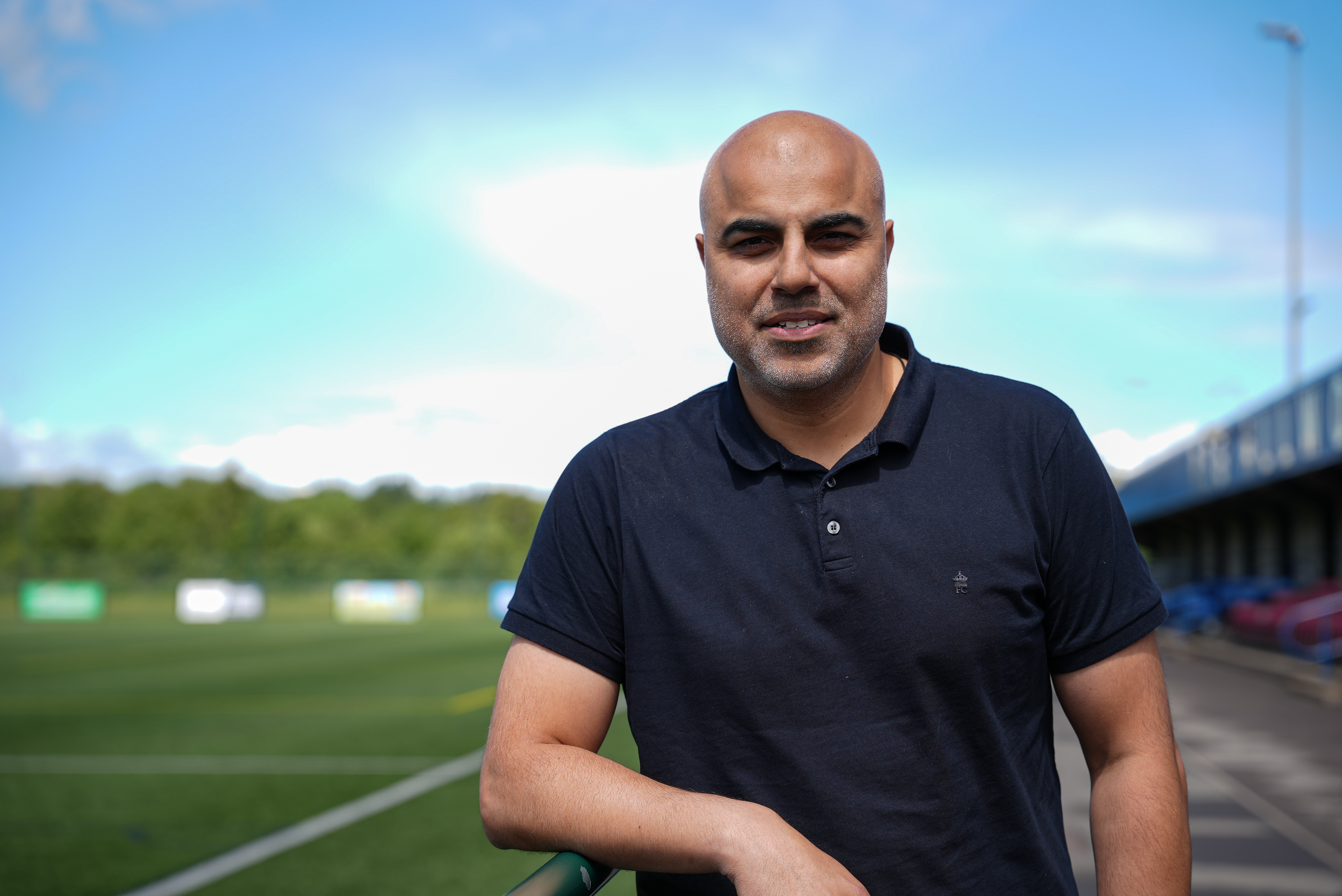 Tahir is standing on a sports field smiling at the camera. 